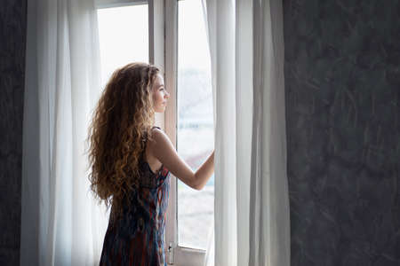 Young woman opening the curtain in the morning after wake up