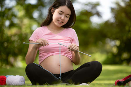 Young Asian pregnant woman knitting a circle scarf with yarn feeling happyの写真素材