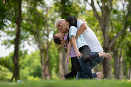 Happy Asian family children having fun and kissing her grandfather on the cheek in the park, summer vacation conceptの写真素材