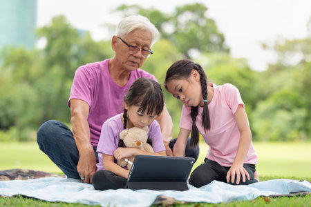 Happy Asian family children using tablet with her grandfather in the parkの写真素材