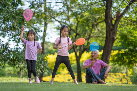 Happy Asian family children having fun and catches a net of insects with her grandfather in the park, summer vacation conceptの写真素材