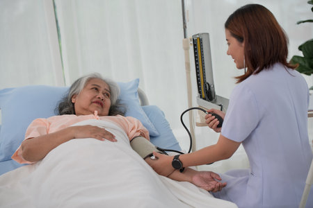 Asian nurse with tonometer measuring senior woman patient's blood pressure at hospitalの写真素材