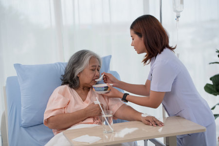 Young Asian nurse feeding breakfast to senior woman patient on bed in hospital ward, elderly care conceptの写真素材