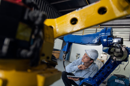 Engineer with helmet safety inspection control a robot arm welding machine with a remote system in...