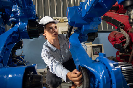 Engineer with helmet safety inspection control a robot arm welding machine with a remote system in...