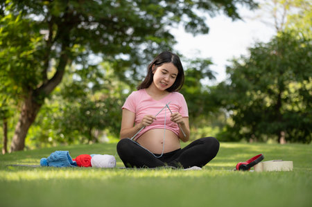 Young Asian pregnant woman knitting a circle scarf with yarn feeling happy