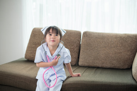 Portrait of a little cute smiling Asian girl wearing a nurse uniform with stethoscopeの写真素材