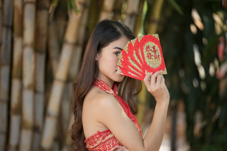 Young happy Asian woman wear cheongsam holding red envelope (red packet) with blessing phrase "gong xi fa cai" text on letter it means "Wish you prosperity" in Chinese New Yearの写真素材