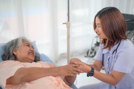 Happy young Asian female nurse gives encouragement to senior woman patient at the hospital ward, elderly care conceptの写真素材