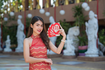 Young happy Asian woman wear cheongsam holding red envelope (red packet) with blessing phrase "gong xi fa cai" text on letter it means "Wish you prosperity" in Chinese New Yearの写真素材