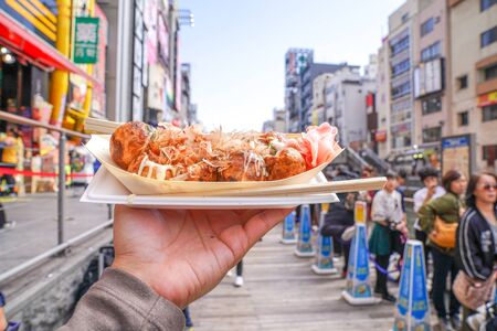 Osaka, Japan - 4 Mar 2018: Takoyaki, the local Japanese octopus meat ball in the hand beside the canal of Osaka., Japan.