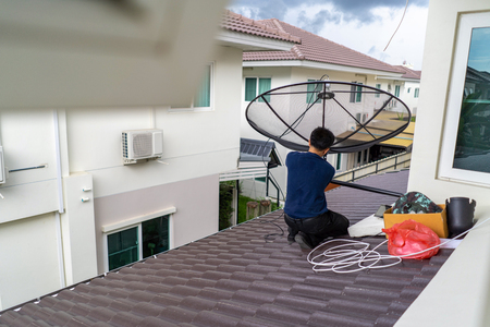 Worker install and set up the digital TV satellite dish on the roof of house.の写真素材