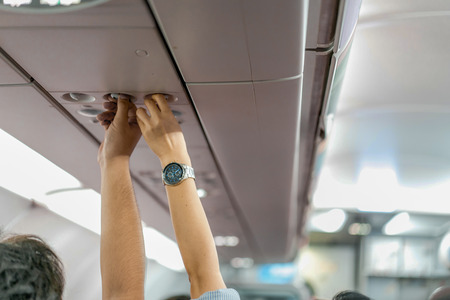Asian couple people cabin crew, hand up to adjust console panel; the air condition, light / lamp above the low cost airline seat.の写真素材