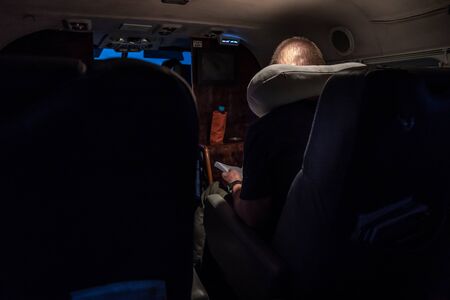 A man read book on the small private jet plane at the night under the light.