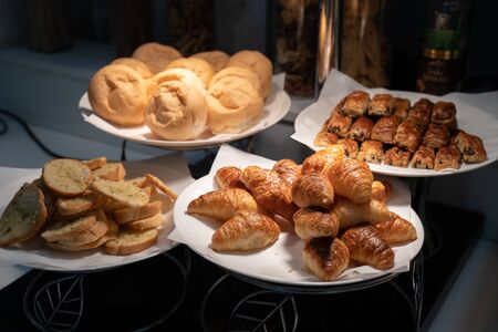 Croissant and bread on paper and white dish in the dark are decorated in tungsten light from lamp.の写真素材