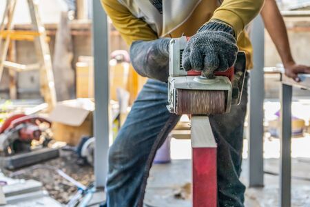 Carpenter is shaving red wood door by his shaving machine in outdoor field with steel pole building structure environment.の写真素材