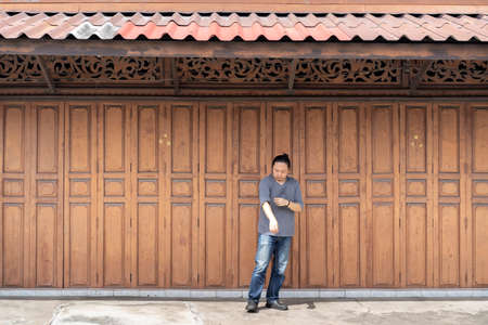 Asian long hair man is standing and posting in front of Classic backdrop wood wall and door in front of Thailand vintage traditional Building.の写真素材