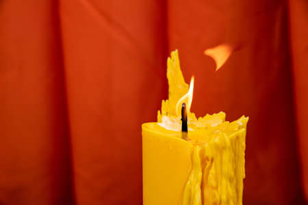 Close up to the melt yellow candle and fire flame with the red curtain background.の写真素材