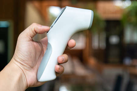 Thermometer Gun in Man's Hand. It's Digital Infrared Sight Temperature Measurement Device on wood...