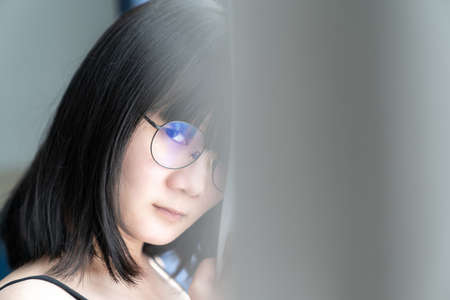 Asian glassese Thai woman looks at the camera and stands behind the gray curtain in the morning.の写真素材