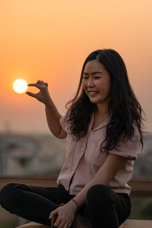 Asian Chinese Thai woman plays with the sun shape on rooftop in twilight time.の写真素材