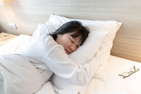 Asian cute young woman in white long arm pajamas lie on her side on the bed