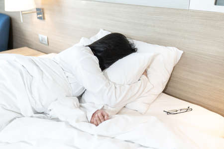 Asian Lady in white long arm t-shirt pajamas lie prone, lie on the stomach in bed with tried and...