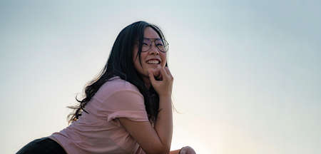 Asian Glasses cute woman postures for photo shooting on the rooftop floor beside cement terrace barracade at twilight time in silhouette angle.の写真素材