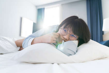 Asian young glasses woman lie on her side on the bed in the morning.の写真素材