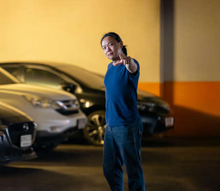Asian long hair man stands and posts in parking car with orange yellow light behind.の写真素材