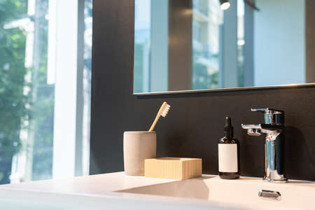 minimal toiletries such as toothbrush, serum bottle and wood storage on white sink and mirror on the...