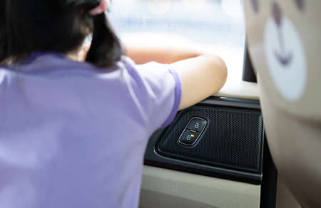 Little Asian 5 years old girl is looking outside through car window mirror with car door lock symbol...