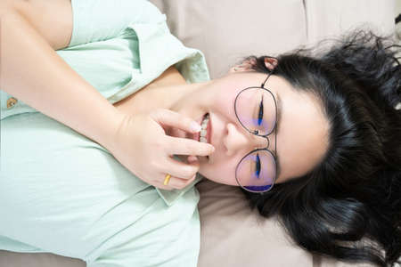 Clouse up to Beautiful glasses Asian woman shy and lie on her back on her bedroom with a pastel green - brown color theme.の写真素材