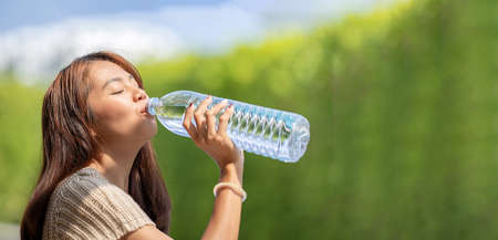 Asian Woman drinks big bottle water in outdoor green bokeh tree background.の写真素材