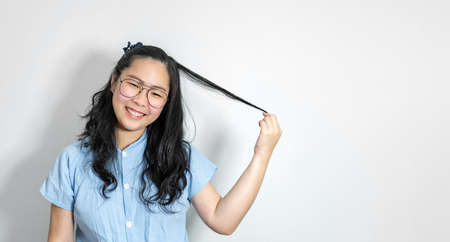A young asian girl touch her hair smoothly with a big smile on her face. She is wearing a light blue shirt and glasses.の写真素材