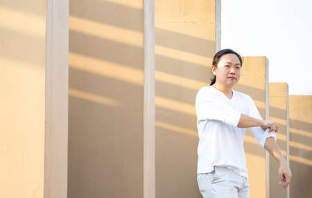 Asian long hair, Man in white long arm t-shirt is standing at the rooftop outdoor field with light brown wall bacgkround.の写真素材