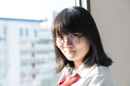 Asian glasses cute woman in blue shirt beside the curtain and window light in bedroom.の写真素材