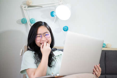 Glasses beautiful Asian woman is working from home with her laptop in the bedroom with a pastel green - brown color theme.の写真素材