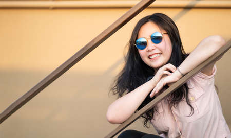 Asian happy woman is sitting on the stair and smile to camera in the sunset time at rooftop of the...