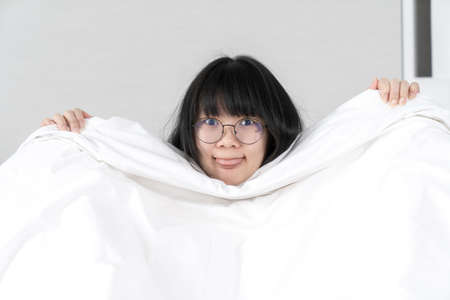 Asian Glasses Girl raises white blanket up and stick her tongue out.