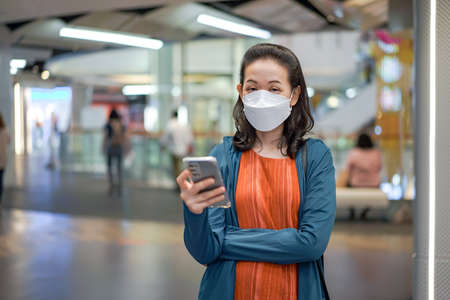 Asian Thai woman wears masks and plays mobile phone in a department or convenience store.