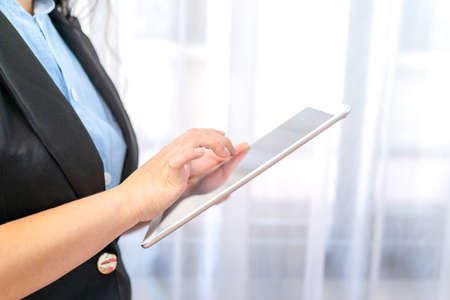 Close up to the White empty screen tablet which hold by Asina women in black suit in front of transparent curtainの写真素材
