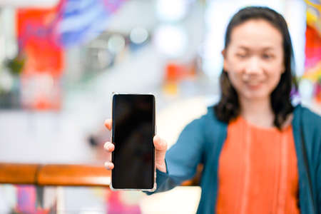 Black screen of mobile in Asian woman hand with blur face in department store background. For mock up website or application on smart phone.の写真素材