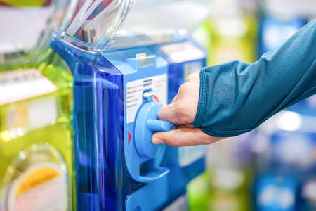 A human hand in a turquoise sweater is twisting a blue gashapon machine to release a figure. In...