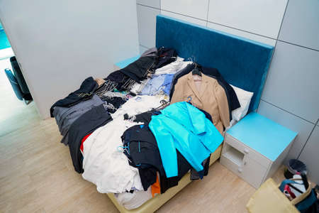 Untidy piles of clothes, arrange on a blue King bed. Women's suits come in a variety of colors, but men's pants were a dark tone color, all of this ready to rearrange in new closet.の写真素材