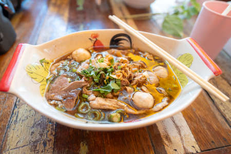 Thai noodle with pork, meatball, pork liver with blood soup in bowl that look like boat on the wood table.の写真素材
