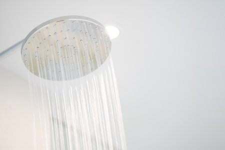 Water was pouring out from a large circular shower in the dimly lit bathroom that has a glass window and can see the view outside.の写真素材