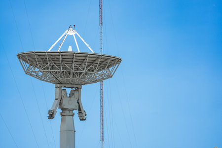 parabolic antenna satellite dish located in front of telecommunication tower with a clear blue sky in the background.の写真素材