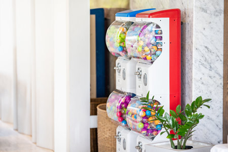 Two red and blue coin operated gachapon cabinets which inside is filled with colorful capsules are located on a light brown marble corridor inside the building.の写真素材