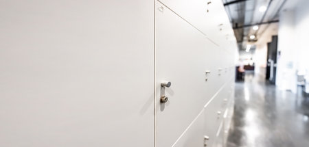Large gray locker with each locker closed located beside corridors inside building are dimly lit.の写真素材